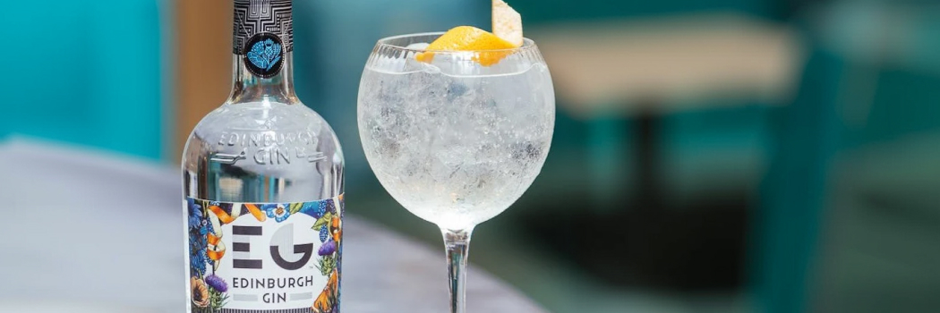 Бутылка классического джина Edinburgh Gin London Dry на фоне цитрусовых и можжевеловых веток